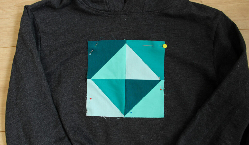 Patchwork quilt block pinned in place on a sweatshirt before sewing