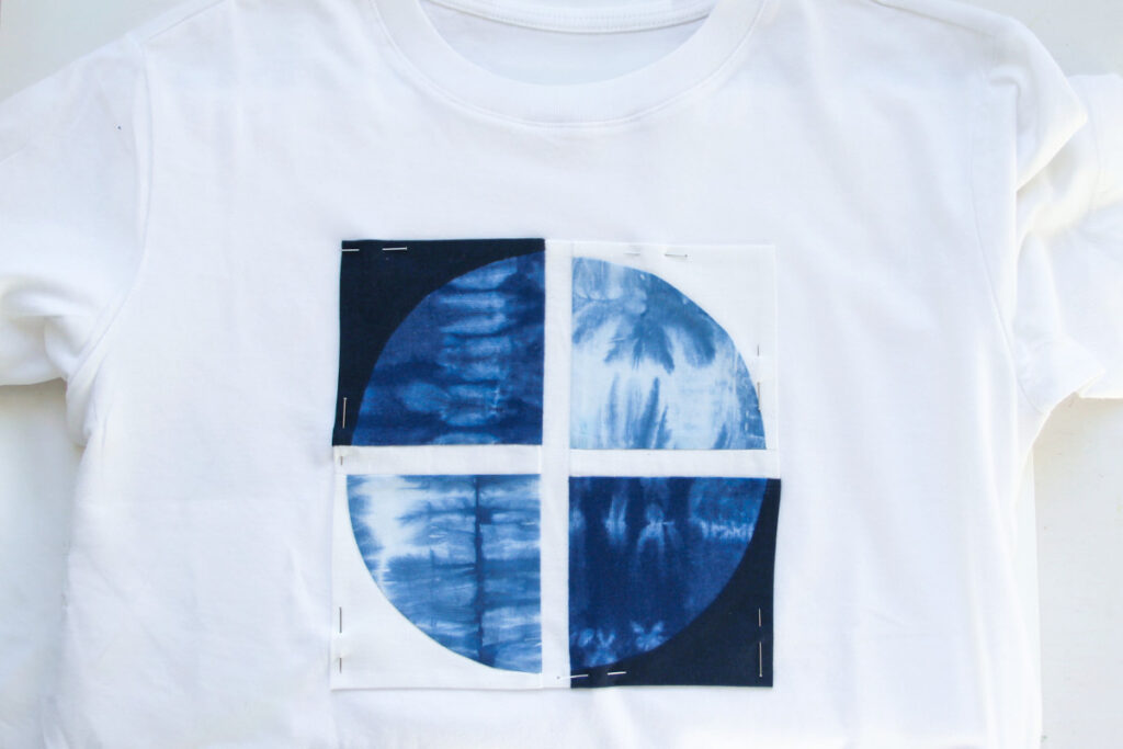 Quilt block pinned to a T-shirt with straight pins for placement.
