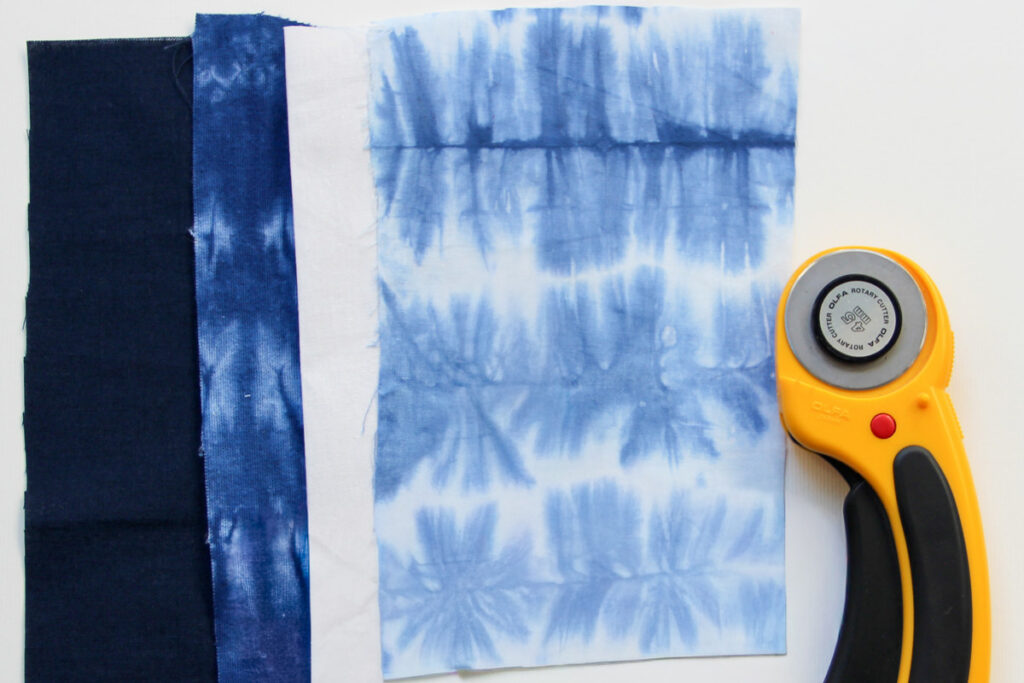 Shibori quilt fabrics stacked on a cutting mat with a rotary cutter.